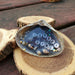 A natural Clam Shell with light blue water and Jersey Girl in the center in white and black letter beads with Shells around the outer edge.