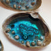 A clam Shell with blue resin and Sand and tiny shells to make a resin Ocean scene inside the shell.  It says Jersey Girl in white and black letter beads.