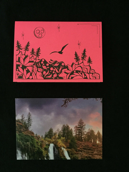 Card features evening nature scene with fish, crab, and seagull on pink paper. Envelope features photograph of a tree-lined cliff with a waterfall and purple sky.