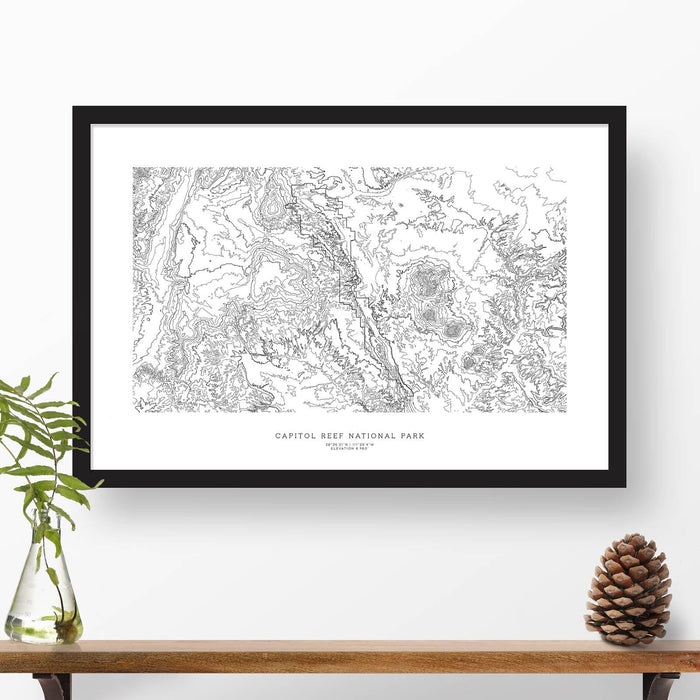 Map wall decor in a black frame. Contour lines of Capitol Reef National Park are drawn on a white background. Text  below the map can be customized to create custom adventure art.
