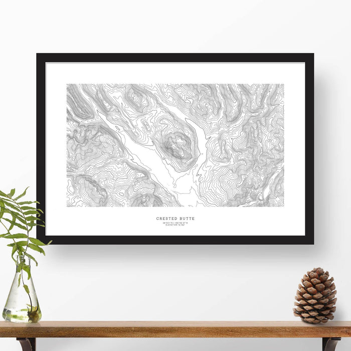 Map wall decor in a black frame. Contour lines of Crested Butte are drawn on a white background. Text  below the ski map art can be customized to create custom adventure art.