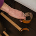 A woman's hand reaching down to a large leather loop basket handle on black-brown kitchen cabinet drawers