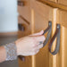 Woman's hand reaching towards a dark brown leather loop cabinet handle. The loop is about the size of her hand. 