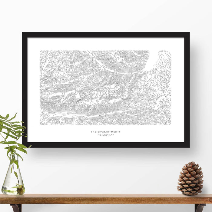 Map wall decor in a black frame. Contour lines of Enchantments, Washington are drawn on a white background. Text  below the map can be customized to create custom adventure art.