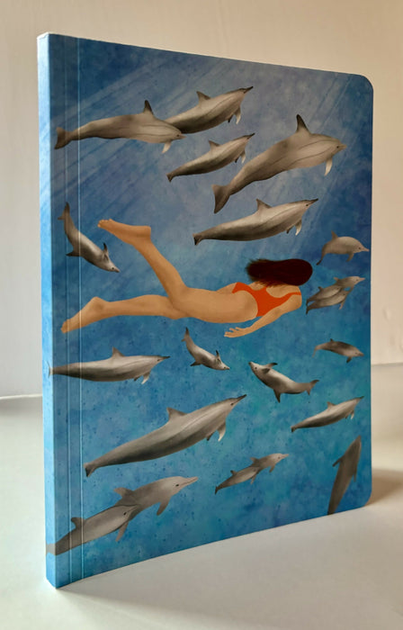 Journal of woman swimming underwater with a pod of dolphins.