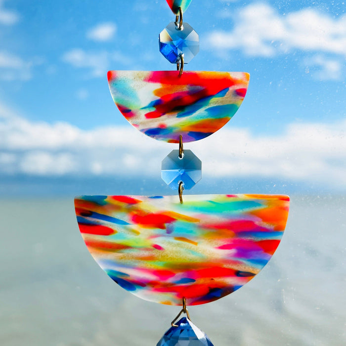 Paint Palette: Colorful handmade suncatcher with bold primary-toned polymer clay pieces in teardrop and arch shapes, paired with translucent blue faceted crystals and a rainbow chain.