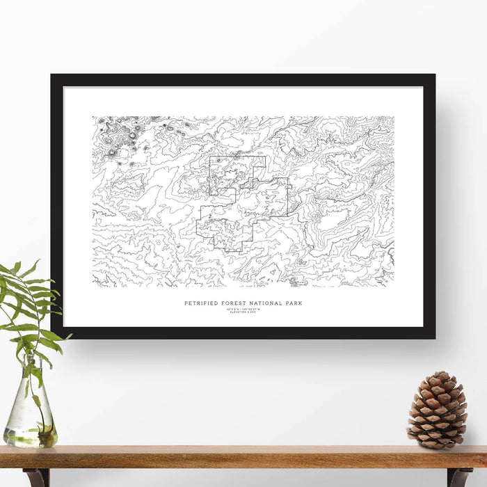 Map wall decor in a black frame. Contour lines of Petrified Forest National Park are drawn on a white background. Text  below the map can be customized to create custom adventure art.