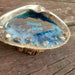 A natural Clam Shell with Love You written in the blue ocean resin with white and black letter beads.  There is Sand, tiny shells, and Gemstones at the outer edge to depict the sandy shore line area.