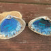 2 Clam Shells recreated with bright ocean blue resin, tiny shells, and white foam for waves.  One says Love You and the other says Love You More with white and black letter beads set inside the blue water (resin) in the shells.