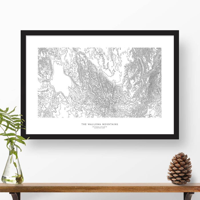 Map wall decor in a black frame. Contour lines of the Wallowa Mountains in Oregon are drawn on a white background. Text  below the map can be customized to create custom adventure art.