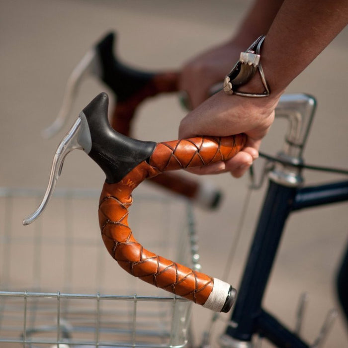 Close-up of a man's hands gripping a classic bicycle drop bar handlebars that are wrapped in braided honey leather, handcrafted and creating a pretty pattern