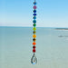 A handmade chakra suncatcher featuring seven stacked polymer clay beads in the colors of the chakras, strung vertically and finished with a hanging faceted glass crystal that reflects rainbows when hit by sunlight. Designed for spiritual, boho, or meditative decor spaces.