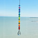 A handmade chakra suncatcher featuring seven stacked polymer clay beads in the colors of the chakras, strung vertically and finished with a hanging faceted glass crystal that reflects rainbows when hit by sunlight. Designed for spiritual, boho, or meditative decor spaces.