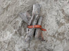 a bundle of gray driftwood logs gathered together and held in place with a tan leather cribbage board belt on a sandy beach