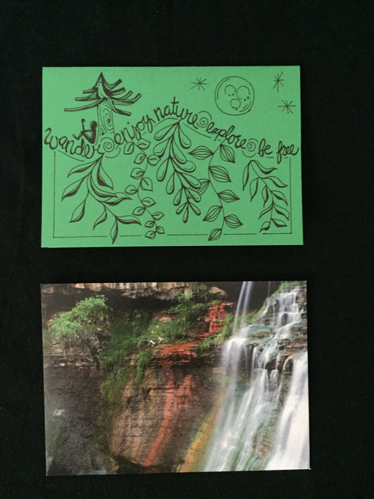 Card features stylized words wander, enjoy nature, explore, be free, along with a nature scene of a person under a tree in the evening. Envelope features photograph of a waterfall.
