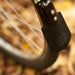 Close-up of a bicycle wheel with a black fender and leather mud flap against a background of blurred autumn leaves