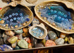 This shows examples of 3 styles of the resin Ocean shells.  THey are sitting on top of a tray of mixed gemstones.