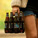 A woman holding a 6-pack of beer in a handsome leather and wood reusable 6-pack carrier