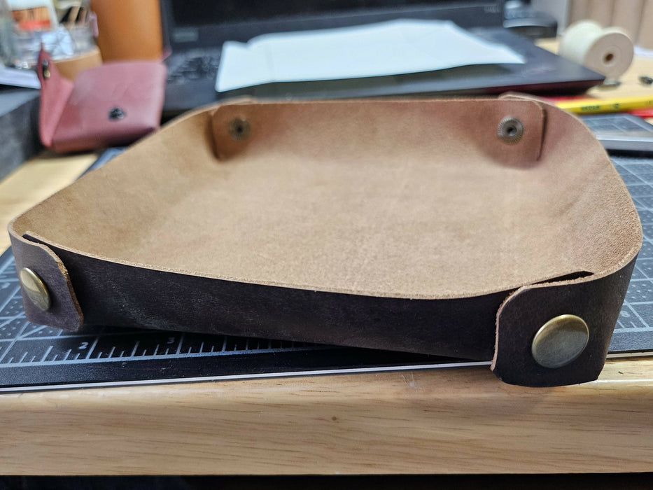 a tray made of brown leather. Rather than the corners pointing outwards, one piece wraps around the corner to snap down, creating more rounded sides.