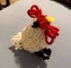 Photo of a tiny knitted chicken. She has cute embroidered details like a comb and wattle, eyes, a beak, a tail, and feet