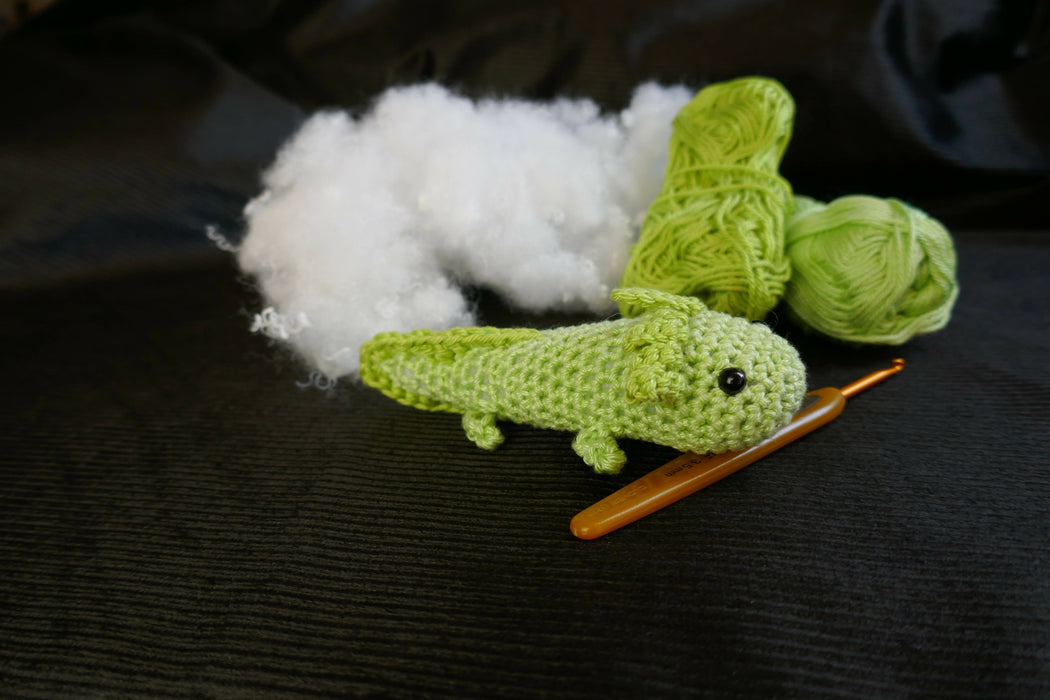 a green axolotl on a black background with some coton tread, padding and a crochet as decors