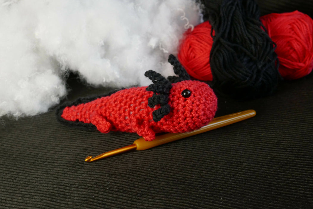 a red axolotl on a black background with some coton tread, padding and a crochet as decors