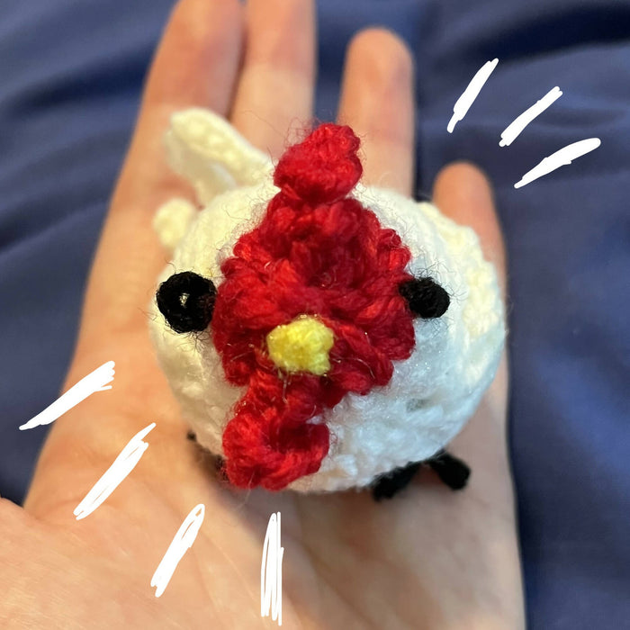Hand holding Fatima the tiny catnip-stuffed chicken, with little embroidered and crocheted details like eyes, a beak, a comb and wattle, wings and a tail. She looks very cute and ready to play!
