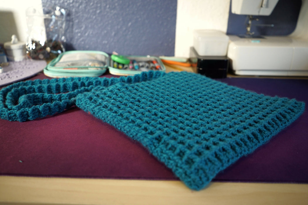 A blue square bag crocheted with a waffle-shaped stitch pattern, made with two sides attached together. Each side has its own strap made from the same yarn.