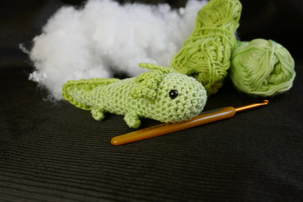 a green axolotl on a black background with some coton tread, padding and a crochet as decors