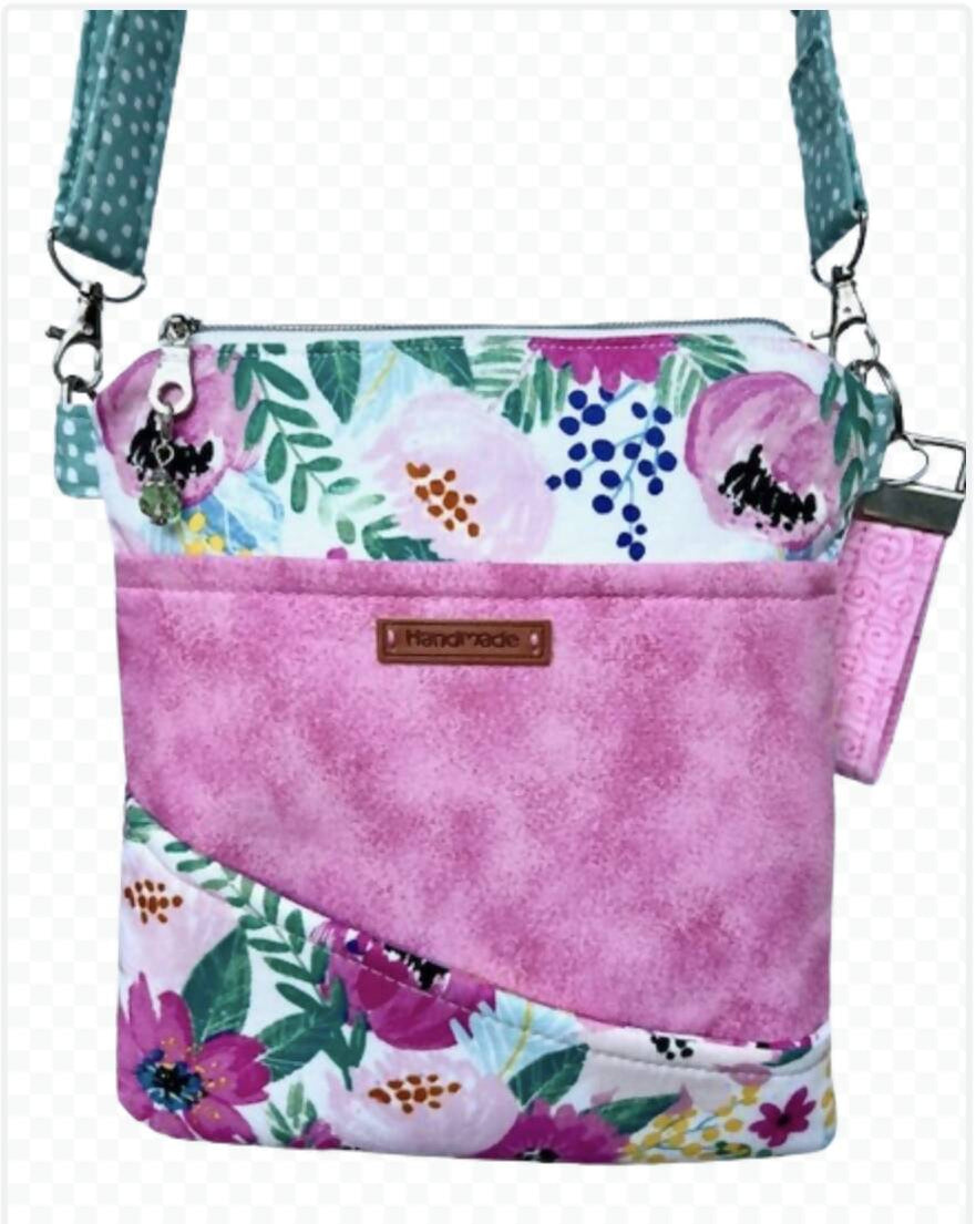 A pink and teal hand-sewn cross-body bag about the size of a large wallet with a pretty poppy and daisy floral pattern