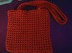 A red square bag crocheted with a waffle-shaped stitch pattern, made with two sides attached together. Each side has its own strap made from the same yarn.