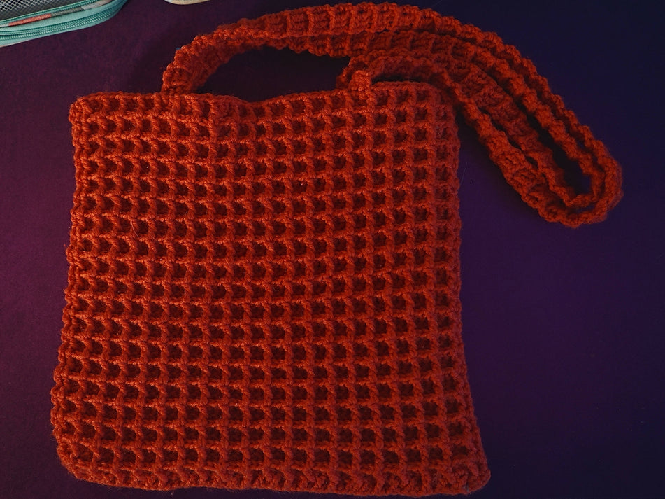 A red, handmade crocheted waffle-stitch tote bag.
