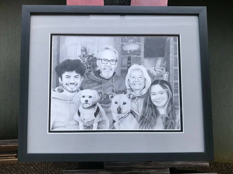 A framed black and white drawing of a 4 person family and their two dogs.