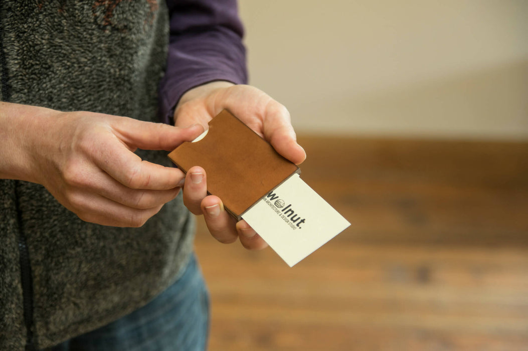 Man pushing a business card out of a leather business card case using a cut out hole for ease of use, a special product feature
