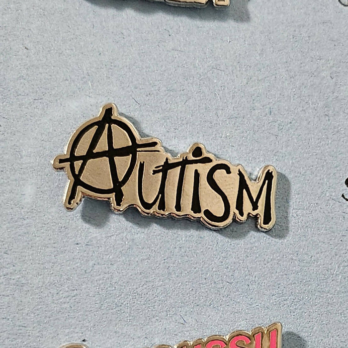 a hard enamel pin with black text that reads autism. the a is styled like the anarchy a