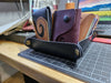 a navy blue leather tray that snaps together at the corners using brass snaps sits on a desk. There are a few card wallets stacked inside it.