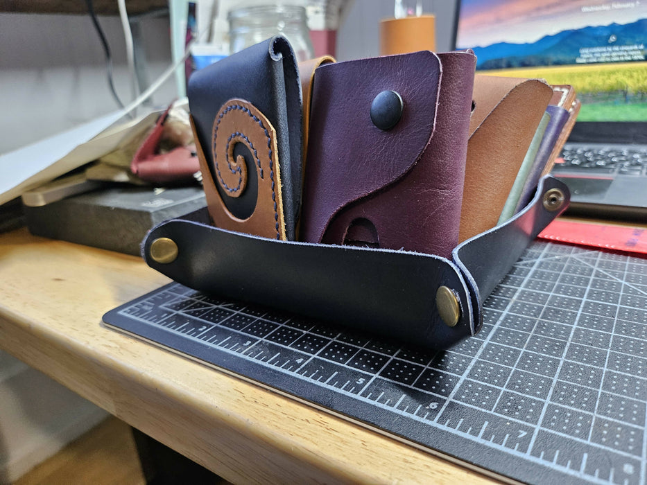 a navy blue leather tray that snaps together at the corners using brass snaps sits on a desk. There are a few card wallets stacked inside it.