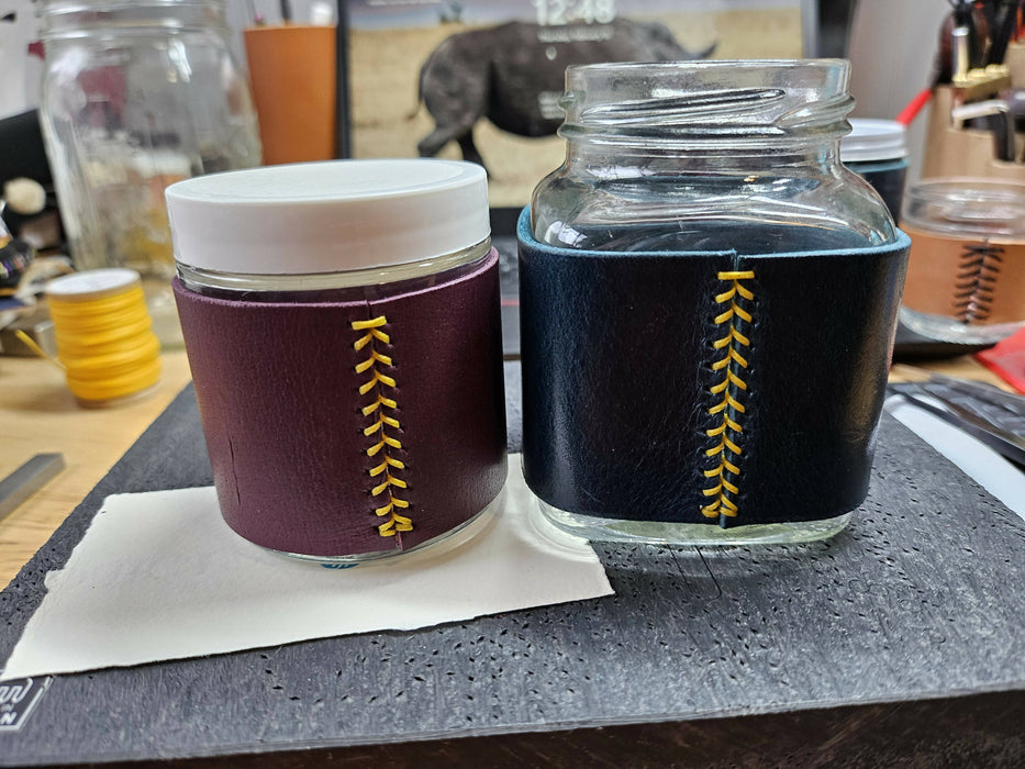 two more jars. the left one is round, with a purple leather wrap and yellow thread. the right is squarish with a blue leather wrap and yellow thread