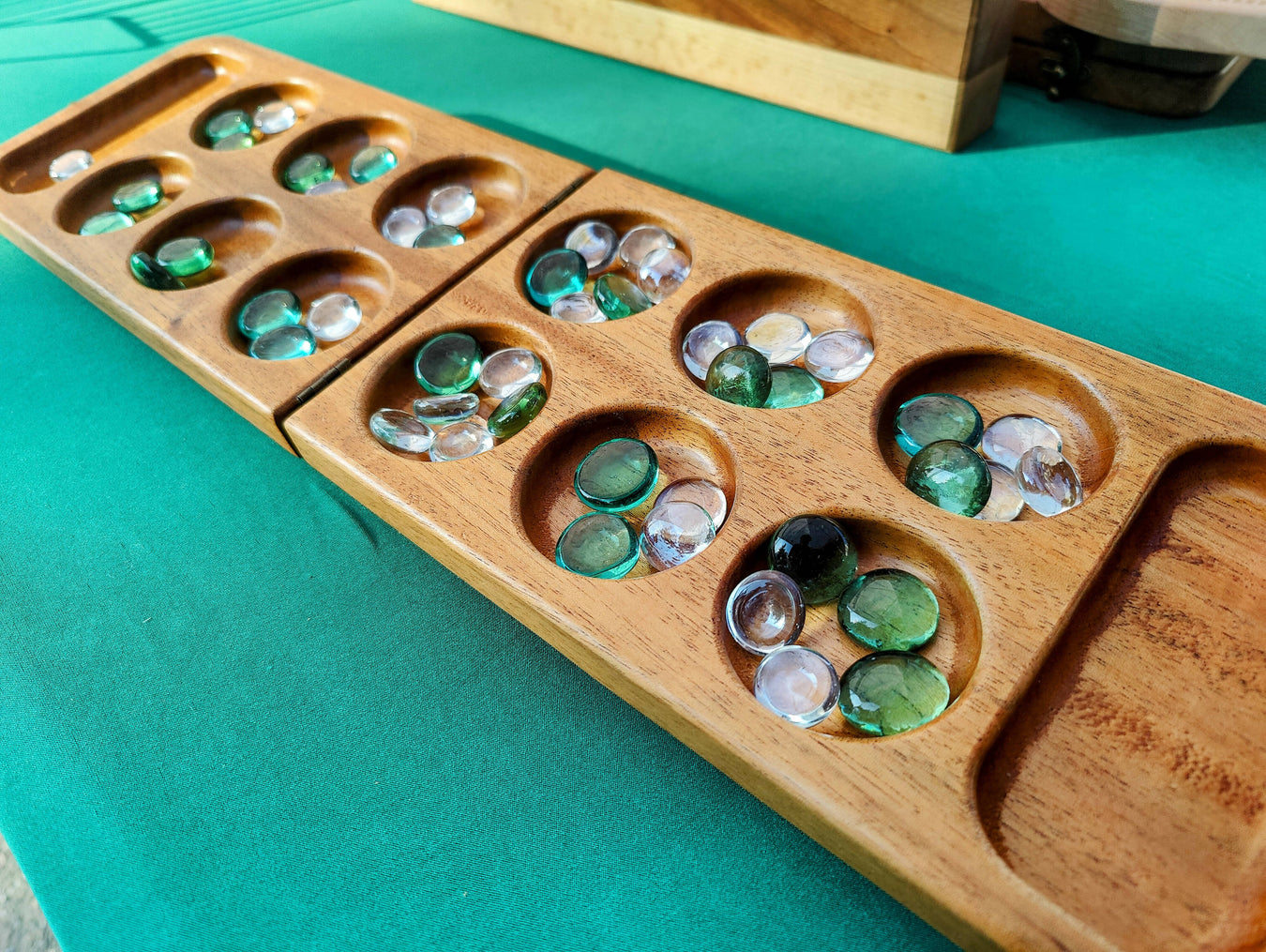 Handmade Wood Mancala Board on a Green Tablecloth with Green and White Glass Stones
