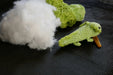 a green axolotl, view on it's back, on a black background with some coton tread, padding and a crochet as decors