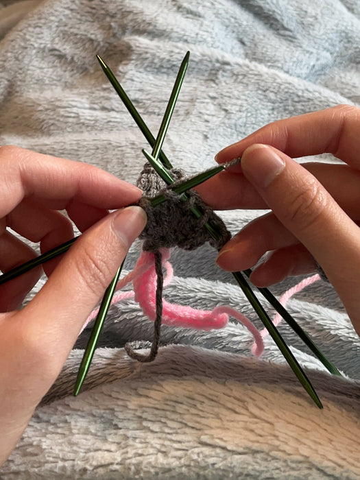 A photo of the artisan's hands, in the process of knitting an opossum from the tail up