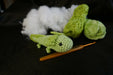 a green axolotl on a black background with some coton tread, padding and a crochet as decors