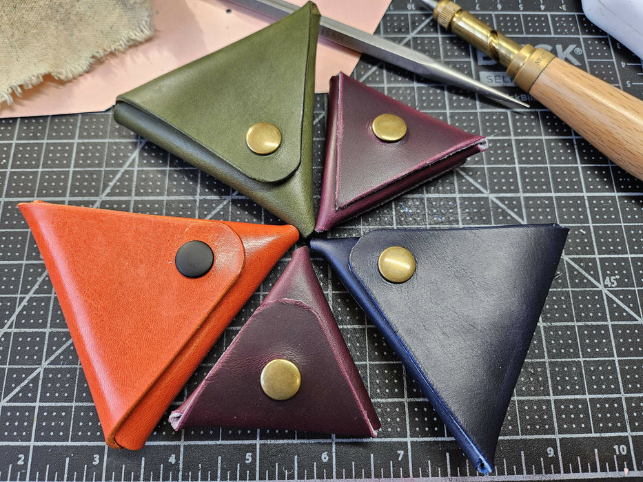 5 triangular leather pouches in a circle. 3 are larger, about palm-sized, in orange, olive green, and blue leather. 2 are smaller, tortilla chip sized, and made of a deep plum leather.